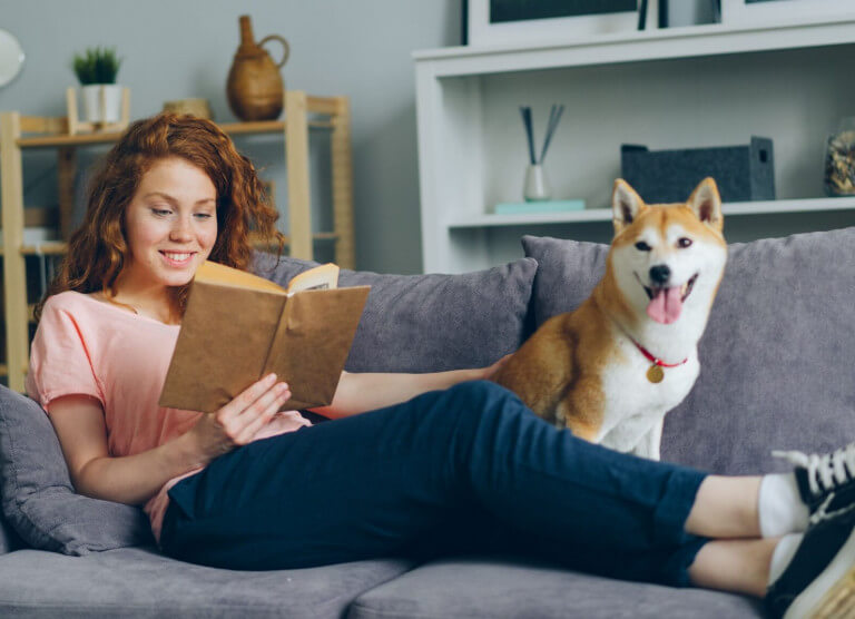 Tüdruk koos koeraga diivanil raamatut lugemas