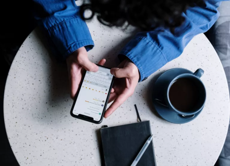telefon käes laua taga istub inimene
